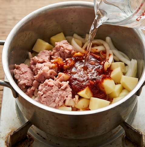 스팸 감자 짜글이 | 밥도둑 대장 조리 단계 4 이미지 - 냄비에 감자, 양파, 으깬 스팸을 넣고 양념장을 올린 뒤 물을 붓는다.